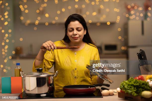 portrait of indian woman enjoying while cooking meal in the kitchen. stock photo - stereotypical homemaker stock pictures, royalty-free photos & images
