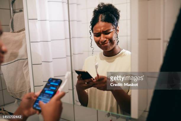 teenager girl with curly hair using smart phone in bathroom at home - brush teeth phone stock pictures, royalty-free photos & images