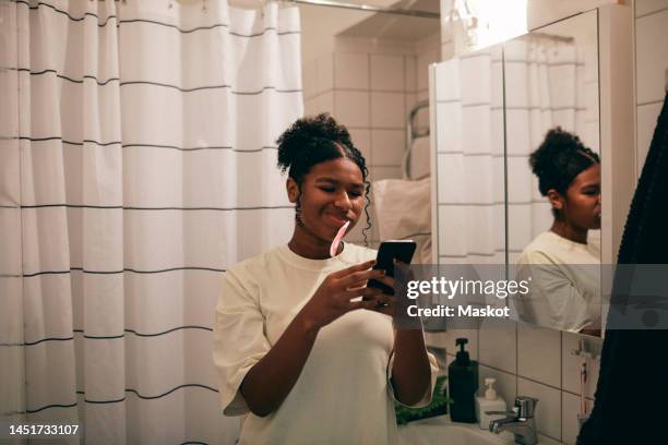 girl brushing teeth while using mobile phone in bathroom - brush teeth phone stock pictures, royalty-free photos & images