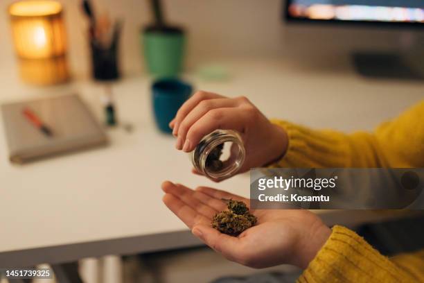 unrecognizable female hand pours medicinal cannabis buds from glass jar into hand - illegal drugs at work stock pictures, royalty-free photos & images