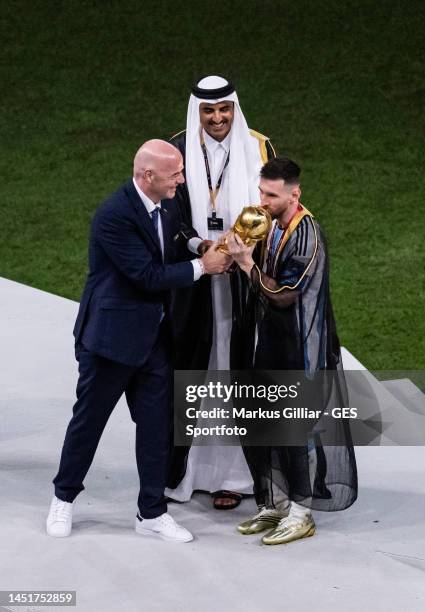 Lionel Messi of Argentina, dressed in a bisht, kisses the World Cup trophy followed by Sheikh Tamim bin Hamad Al Thani , Emir of Qatar and FIFA...
