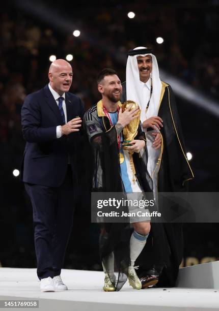 President Gianni Infantino, Emir of Qatar Sheikh Tamim bin Hamad Al Thani and Lionel Messi of Argentina - holding the World Cup and wearing a...