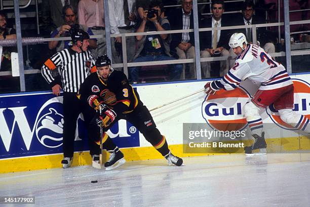 Bret Hedican of the Vancouver Canucks skates with the puck as Stephane Matteau of the New York Rangers tries to hook him as referee Terry Gregson...