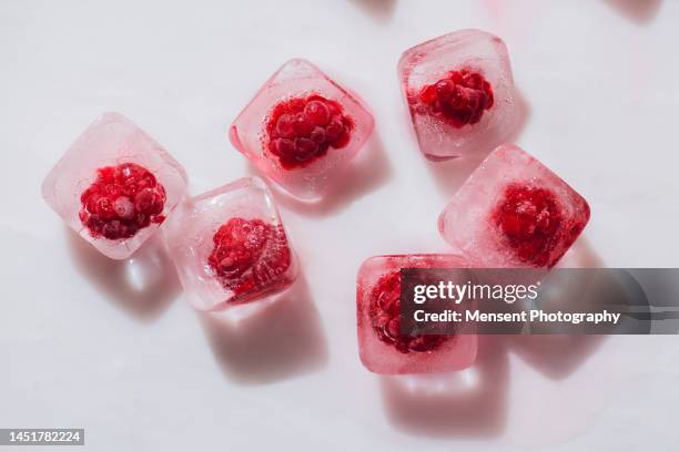 red raspberries in frozen a cubes ice on marble surface background, raw fruits background - icecubes stock-fotos und bilder