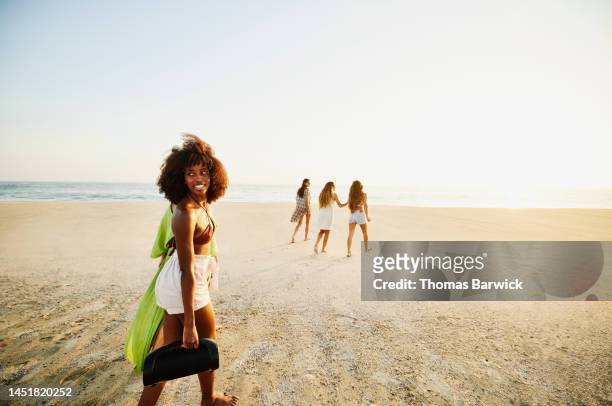wide shot of woman carrying speaker while walking with friends on beach - black dress party stock pictures, royalty-free photos & images