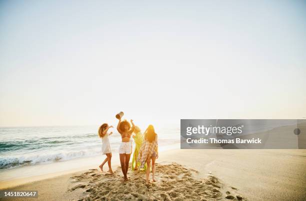 wide shot of female friends dancing on tropical beach at sunset - tropical music stock-fotos und bilder