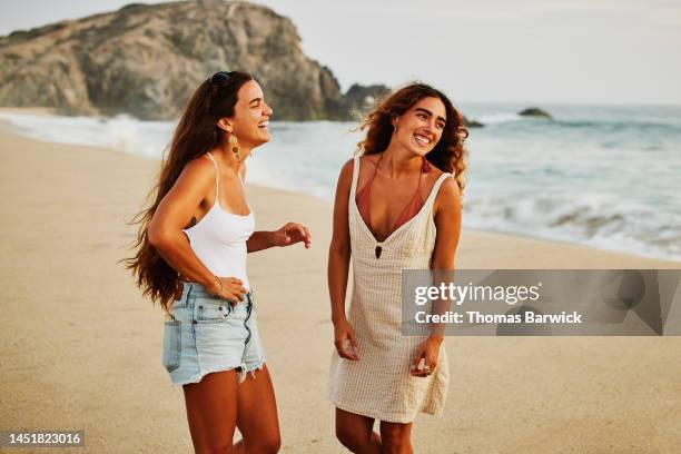 medium shot of laughing friends hanging out on tropical beach at sunset - tre quarti foto e immagini stock