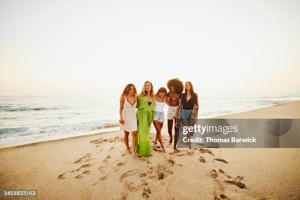 wide shot of smiling friends embracing on tropical beach at sunset - grünes kleid stock-fotos und bilder