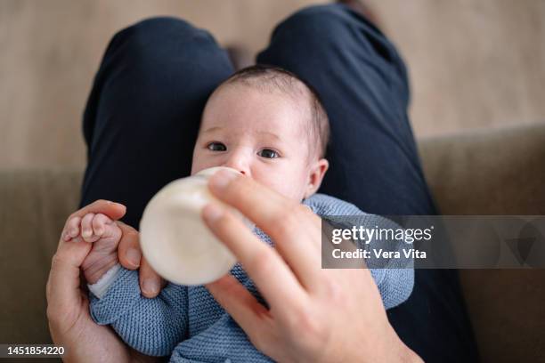 portrait of caucasian baby with unrecognizable father feeding milk bottle in foreground - milchpulver stock-fotos und bilder