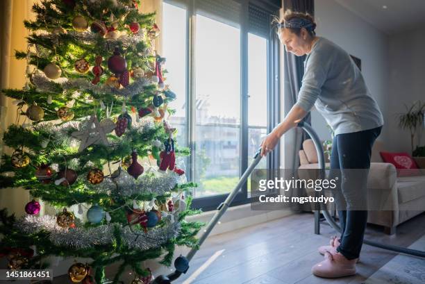 mature woman with vacuum cleaner indoors at home at christmas time - vacuum cleaner woman stockfoto's en -beelden