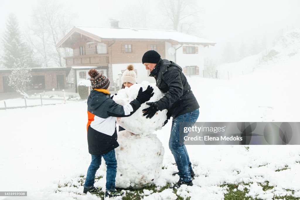 Children make a snowman with dad at the weekend. Dad helps build a snowman out of snow globes. Family activity, time together with family