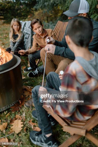 dad helping kids roast marshmallows around fire - marsh mallows stock pictures, royalty-free photos & images
