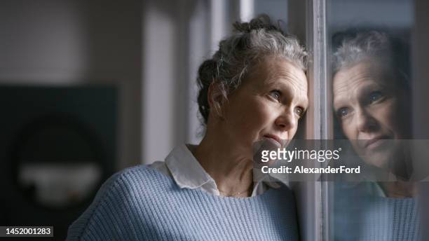 elderly woman, window reflection and depression while thinking, wonder and mental health in home. senior lady, retirement anxiety and sad in house with stress, mirror and depressed in san francisco - angry woman concept stock pictures, royalty-free photos & images