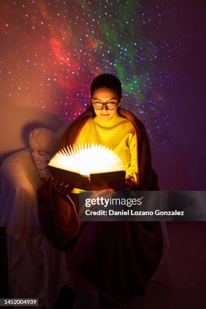 young attentive woman reading a magical illuminated book at home. - literature fotografías e imágenes de stock