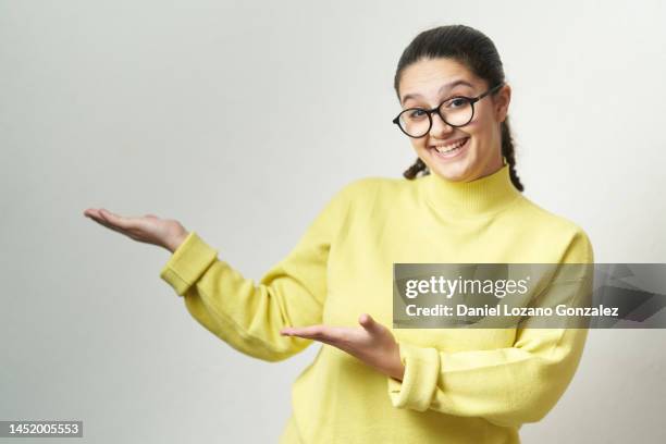 young woman looking at camera and smiling while showing something standing on an isolated background. - werbemittel stock-fotos und bilder