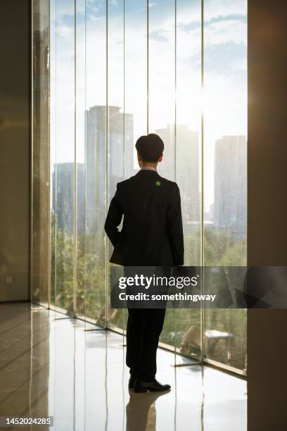 asian businessmen look at their watches in front of the office window - rim light portrait stock pictures, royalty-free photos & images