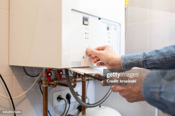 hombre blanco baja la temperatura de la caldera de gas de su casa por la crisis energética - calentador fotografías e imágenes de stock