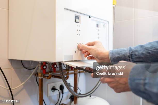 l'uomo bianco abbassa la temperatura della caldaia a gas nella sua casa a causa della crisi energetica - caldaia foto e immagini stock