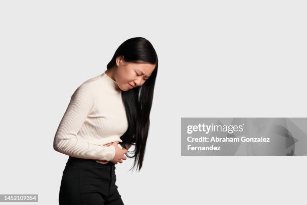 asian woman with stomach pain touching her belly - portrait white background male foto e immagini stock