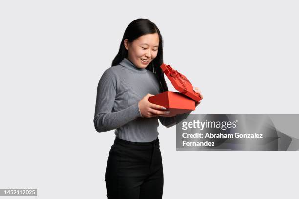 happy asian woman opening a gift in a red box - dream deliveries stockfoto's en -beelden