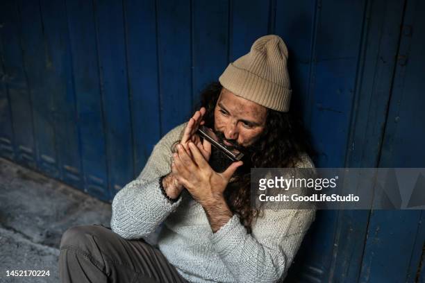 obdachloser spielt mundharmonika - sad busker stock-fotos und bilder