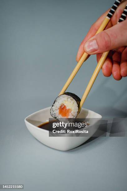 chopsticks dipping a tasty roll into a bowl with soy sauce on a white plate. - dipping sauce stock-fotos und bilder