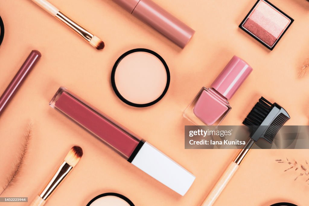 Set of different makeup accessories on beige, brown background. Cosmetic products for skin care. Eyeshadow, blush, face powder, nail polish, brushes and lipstick.