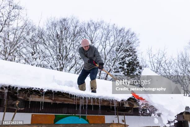 senior man shoveling snow off roof - winter snow shovel stock pictures, royalty-free photos & images
