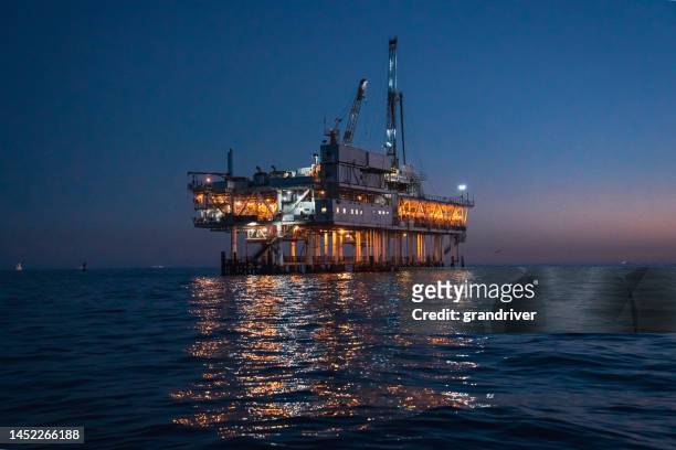 night time offshore oil rig drilling and fracking operation, brightly lit, on calm seas - drillinge stock pictures, royalty-free photos & images