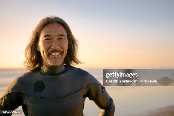 portrait of smiling senior standing on beach next to morning sun - surfer portrait fotografías e imágenes de stock