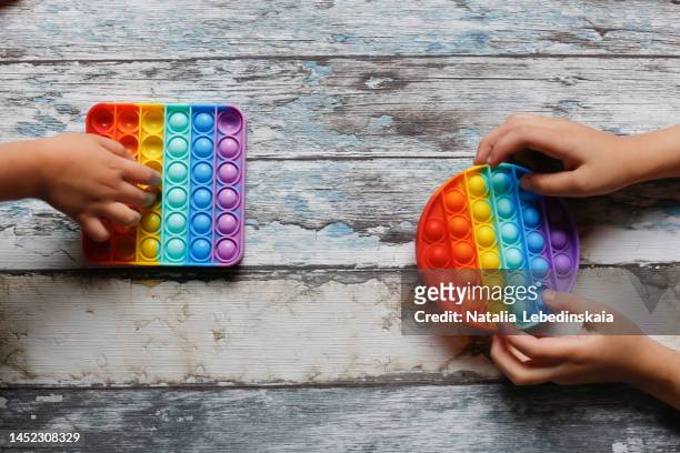 children's hands press on pop it on wooden background. cute children playing with the pop it fidget. - fidget spinner stock pictures, royalty-free photos & images