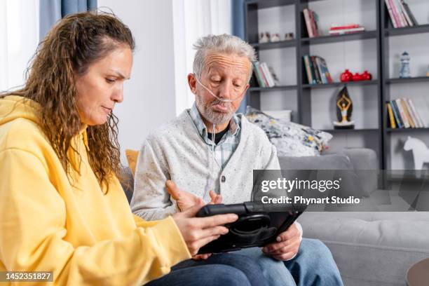 hombre mayor recibe ayuda en tableta digital de una mujer joven - tubo de oxígeno fotografías e imágenes de stock