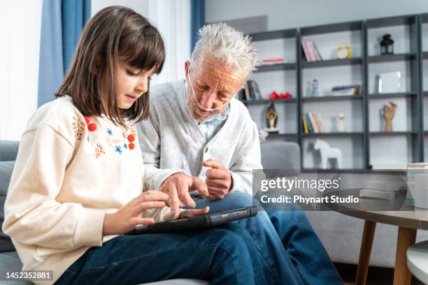 un homme âgé prend de l’aide dans une tablette numérique de sa petite-fille - équipement d'assistance respiratoire photos et images de collection