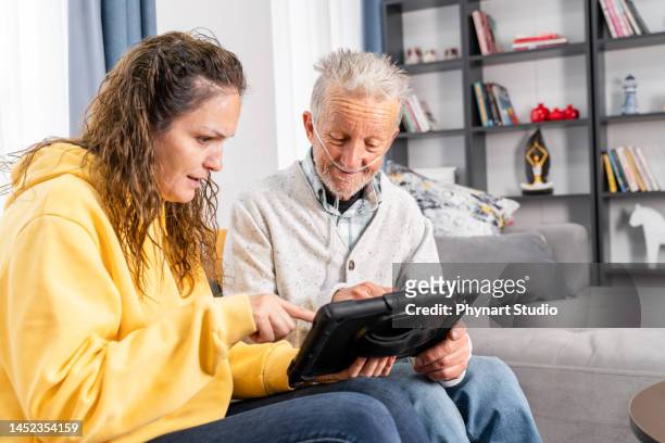 älterer mann nimmt hilfe in digitalem tablet von einer jungen frau - it is finished stock-fotos und bilder