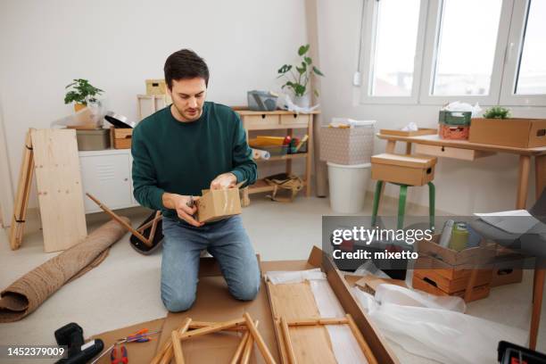 giovane uomo casualmente vestito tenendo scatola con viti per il montaggio dello scaffale in un moderno appartamento accogliente - furniture maker foto e immagini stock