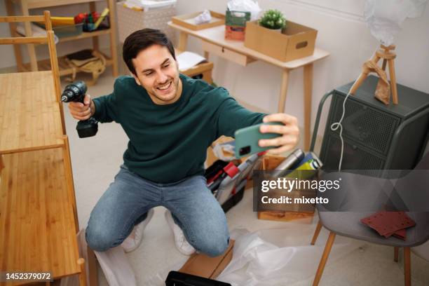 young handsome man taking selfie while assembling shelf at his new apartment - furniture instructions stock pictures, royalty-free photos & images