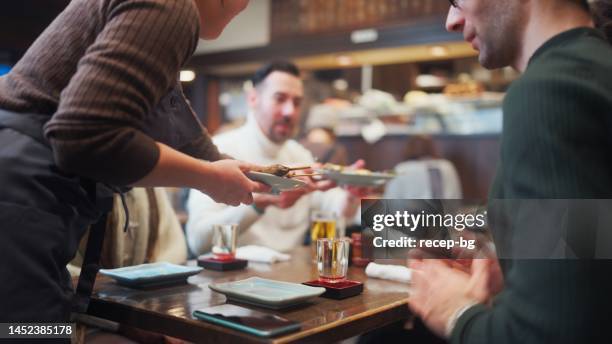 waitress serving japanese food to group of multi-ethnic tourist friends in japanese style pub izakaya - japanese restaurant stock pictures, royalty-free photos & images