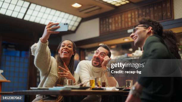 grupo de amigos turísticos multiétnicos disfrutando de bebidas y comida en el pub de estilo japonés izakaya y tomando selfies con el teléfono inteligente - black and white food fotografías e imágenes de stock