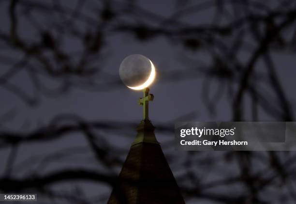 Percent waxing crescent moon lit with earthshine sets behind a church on December 25 in Jersey City, New Jersey.