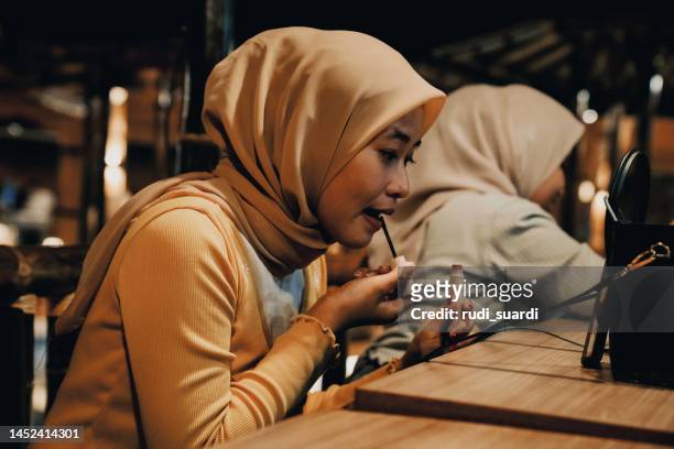 zwei muslimische frauen tragen lippenstift während des abendessens im restaurant auf - muslims prepare for eid in indonesia stock-fotos und bilder