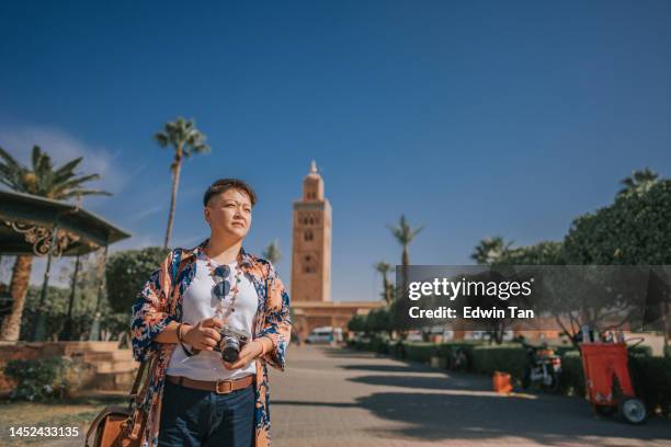 asian chinese tourist in front of koutoubia mosque looking away - minaret stockfoto's en -beelden