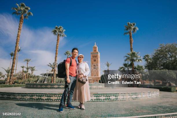portrait asian chinese tourist couple looking at camera in front of fountain , koutoubia mosque, morocco - marrakesh stockfoto's en -beelden