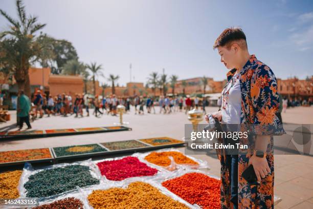 curious asian chinese female tourist looking at colourful dried flowers on a market in a bazaar in marrakech, morocco, north africa - marrakech stockfoto's en -beelden
