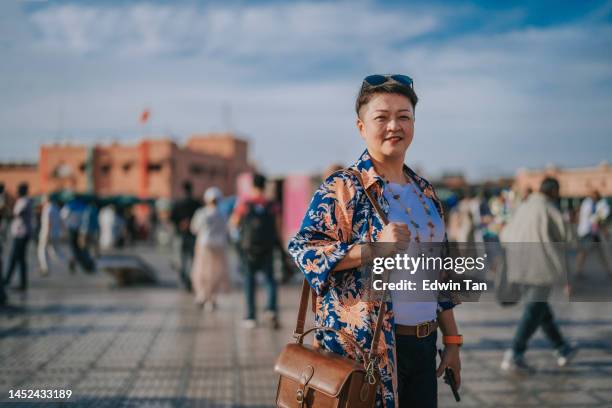 asian chinese female tourist standing looking at camera smiling  in front of djemaa el fna square, marrakech, morocco - market square stock pictures, royalty-free photos & images