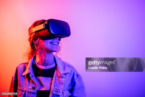 young black woman playing game using vr glasses, enjoying 360 degree virtual reality headset for gaming, isolated on background with neon lights - headwear stockfoto's en -beelden