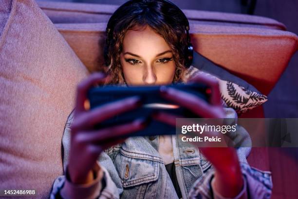 plan rapproché d’une jeune femme adorable jouant à un jeu sur un téléphone portable allongée sur un canapé - jeu mobile photos et images de collection
