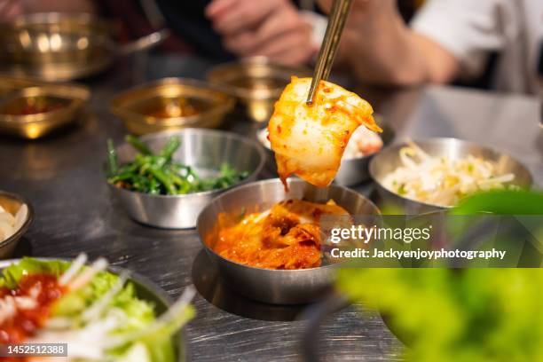 close up of woman serving fresh kimchi on plate while having meal in a korean restaurant - korean culture stock-fotos und bilder