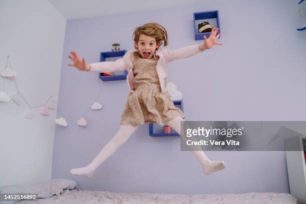 caucasian little girl jumping high with arms wide open in bedroom - jumping on bed stockfoto's en -beelden