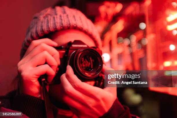 young woman takes photo with vintage camera in neon-lit room. - photographer stock pictures, royalty-free photos & images