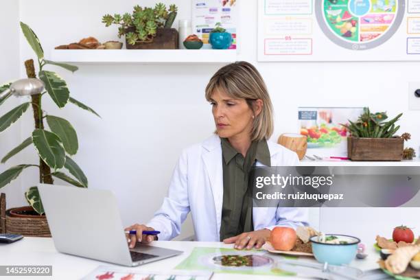 female nutriotionist doctor in her office working at her laptop - nutritionist stockfoto's en -beelden